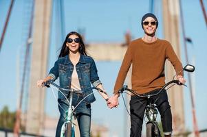 Enjoying their active date. Beautiful young couple riding bicycles along the bridge and smiling photo