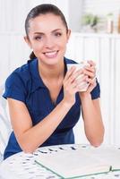 Woman relaxing in cafe. Beautiful young woman holding cup with hot drink and smiling while sitting in cafe photo