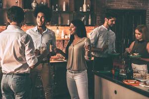 fiesta en casa con los amigos más cercanos. grupo de jóvenes alegres que disfrutan de una fiesta en casa con bocadillos y bebidas mientras se comunican en la cocina foto