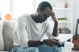 Another loss Handsome young African man holding hand on his face while sitting on the sofa at home photo