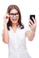 Selfie Attractive young woman holding mobile phone and making photo of herself while standing against white background