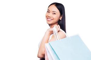 Shopping is the best female occupation Side view of beautiful young Asian woman in pretty dress looking at camera and holding shopping bags while standing against white background photo