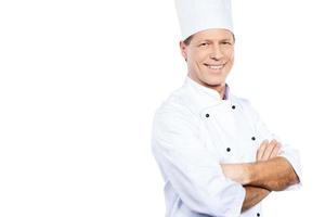 cocinar es mi pasión. chef maduro confiado en uniforme blanco con los brazos cruzados y sonriendo mientras está de pie contra el fondo blanco foto