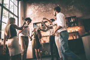 Enjoying party with friends. Low angle view of cheerful young people dancing and drinking while enjoying home party on the kitchen photo