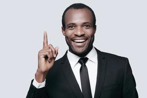 I have an idea Handsome young African man in formalwear pointing up and smiling while standing against grey background photo