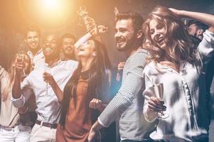 les encanta bailar. grupo de hermosos jóvenes bailando con flautas de champán y luciendo felices foto