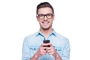 Smart phone for smart people Handsome young man in shirt looking at camera and holding mobile phone while standing against white background photo