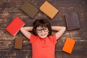 I love studying Top view of a little boy lying on the floor and smiling while books laying all around him photo