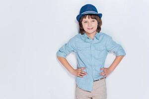 Stay cool Cheerful little boy wearing hat and holding hands on hips while standing against white background photo