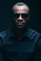 Cool and handsome. Portrait of handsome young African man in sunglasses looking at camera while being in front of black background photo