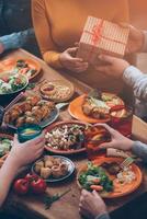 Birthday present. Top view of group of people having dinner together while man giving a present box to women photo