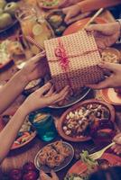 Happy birthday Top view of group of people having dinner together while male hands giving a present box to some women photo