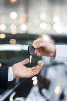 Here is your key Close up of man giving key to the car owner while standing in front of a car photo