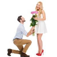 They are as beautiful as you Full length of man standing at his knee and giving a bouquet of pink roses while both isolated on white background photo