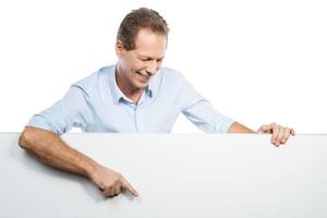 Look at that Happy mature man leaning at the copy space and pointing it with smile while standing against white background photo