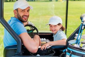 Father and son  the best team. Cheerful young man and his son looking at camera while sitting in golf cart photo