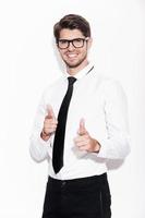 I choose you Cheerful young man pointing at camera and smiling while standing against white background photo
