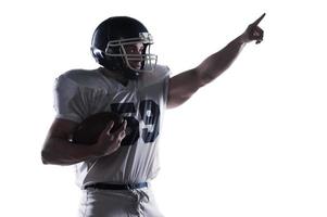 Over there  American football player holding ball and pointing away while standing against white background photo