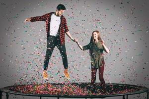tiempo de diversión toma en el aire de una hermosa pareja joven y alegre saltando en un trampolín junto con confetti a su alrededor foto