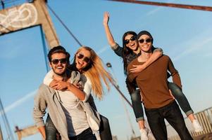 We just want to have fun Two handsome young men piggybacking their girlfriends and smiling while walking along the bridge photo