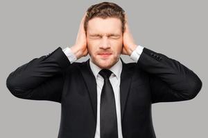 This is too loud Frustrated young man in formalwear holding head in hands and keeping eyes closed while standing against grey background photo