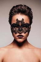 Beauty in mask. Portrait of beautiful young shirtless woman in black mask looking at camera while standing against grey background photo