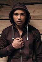 Power inside. Confident young African man in hooded shirt looking at camera while standing against wooden background photo