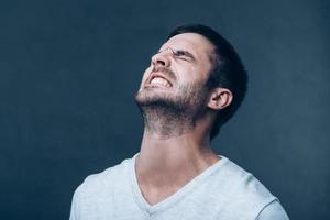 Oh no Frustrated young man keeping eyes closed and expressing negativity while standing against grey background photo