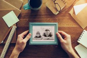 My son is my inspiration. Close-up top view of man holding photograph of himself and his son over wooden desk with different chancellery stuff laying around photo