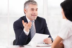 I think you are the perfect candidate Smiling mature man in formalwear talking to young woman sitting in front of him and gesturing photo