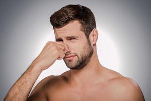 This awful smell Portrait of frustrated young shirtless man holding fingers on nose and making a face while standing against grey background photo