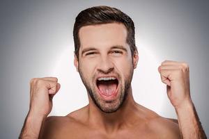 sintiéndose tan feliz retrato de un joven feliz sin camisa mirando a la cámara y gesticulando mientras está de pie contra un fondo gris foto