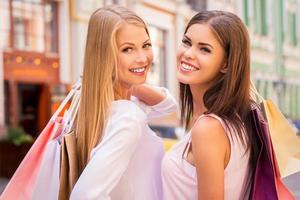 Enjoying shopping together. Rear view of two beautiful young women holding shopping bags and looking over shoulder with smile while standing outdoors photo