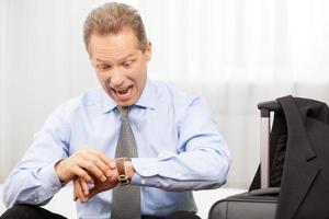 Late again Surprised grey hair man in shirt checking the time while sitting on the bed photo