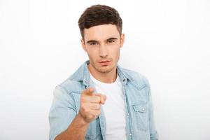 I choose you Serious young man pointing at camera while standing against white background photo