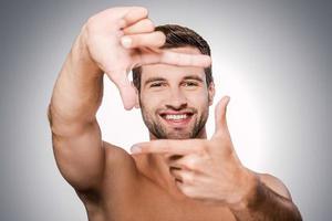 Focus on me Portrait of handsome young shirtless man looking at camera and gesturing finger frame while standing against grey background photo
