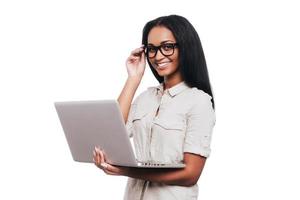 How may I help you Confident young African woman holding laptop and smiling while standing against white background photo