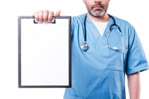 Copy space on his clipboard. Confident mature doctor looking at camera and showing clipboard with copy space on it while standing isolated on white photo