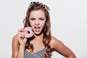 ¿Quieres un bocado hermosa mujer joven sosteniendo un donut mordido mientras está de pie contra el fondo blanco foto