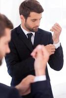 Everything should be perfect. Handsome young man in formalwear adjusting his sleeves while standing against mirror photo