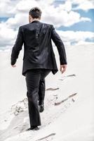 He is on his way to success. Rear view of young man in formalwear rising up by desert dune photo