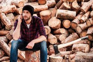 The work is done Handsome young forester talking on the mobile phone and looking away while sitting on the log photo