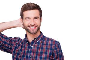 casualmente guapo. retrato de un joven apuesto con una camisa casual sosteniendo la mano detrás de la cabeza y sonriendo mientras está de pie aislado en blanco foto