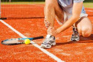 Sports injury. Close-up of tennis player touching his leg while sitting on the tennis court photo