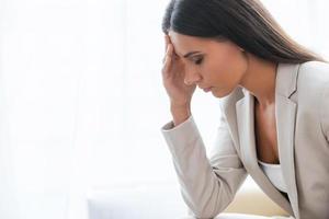 Tired and depressed businesswoman. Side view of depressed young businesswoman in suit touching head with hand and keeping eyes closed while sitting at the chair photo