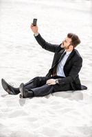 In search of signal. Frustrated young businessman searching for mobile phone signal while sitting on sand in desert photo