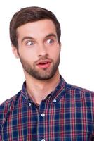 Shocked about... Portrait of shocked young man keeping mouth open while looking away while standing isolated on white photo