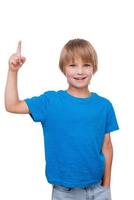 Look over there. Cheerful little boy pointing up and smiling while standing isolated on white photo