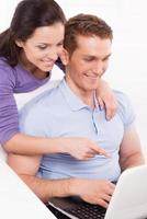 Surfing the net together. Happy young loving couple sitting on the couch and looking at laptop while woman pointing monitor and smiling photo