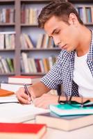 estudiando duro. vista lateral de un joven confiado investigando mientras está sentado en el escritorio de la biblioteca foto